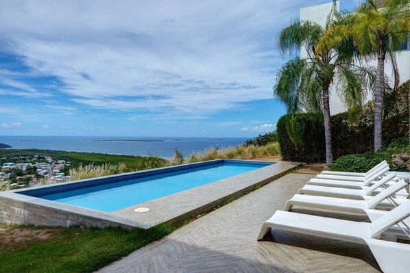 A swimming pool with lounge chairs, a view of the ocean, and a clear sky. - 5BR Villa | Private Pool + Walk-Out Kitchen | Near Seven Seas Beach | Sleeps 14 (Fajardo)