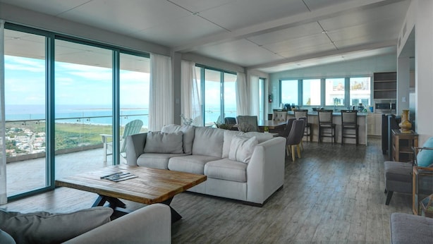 Un vaste espace de vie comprenant un grand canapé, une table basse et un coin repas avec des tabourets de bar.