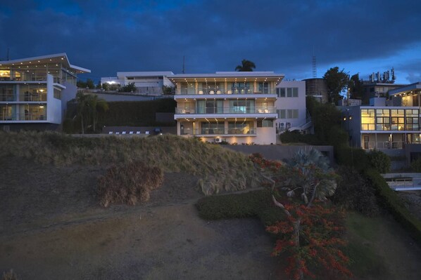 A multi-story modern house with large windows and a balcony, surrounded by landscaped gardens. - 5BR Villa | Private Pool + Walk-Out Kitchen | Near Seven Seas Beach | Sleeps 14 (Fajardo)