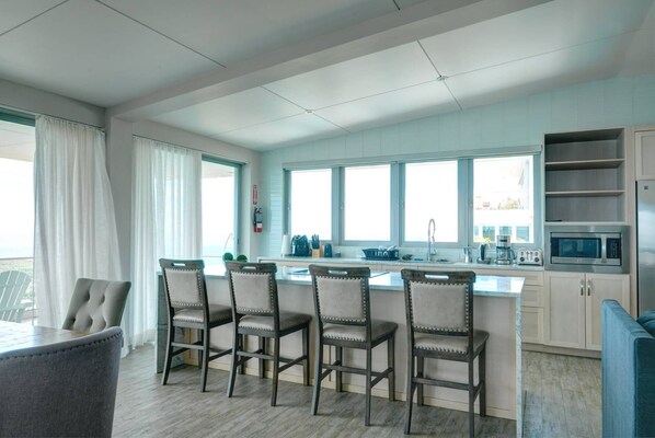 Una cocina moderna con una isla central, taburetes de bar y vistas al mar a través de amplios ventanales.