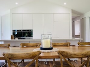 A modern kitchen with white cabinets, a built-in oven, and a dining area with wooden chairs and a glass table. - One Acre Retreat Silverleaves Phillip Island Walk to Beach & Cowes (Silverleaves)