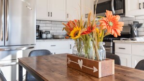 A kitchen with white cabinets, a stainless steel refrigerator, and a wooden table with a vase of flowers. - charming 2-bedroom pioneer home near brian head ski resort and national parks in parowan, utah (Parowan)