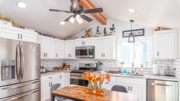 A modern kitchen with white cabinets, stainless steel appliances, a wooden dining table, and a ceiling fan. - charming 2-bedroom pioneer home near brian head ski resort and national parks in parowan, utah (Parowan)