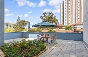 Relax on the rooftop terrace surrounded by lush greenery and potted plants, with a table and chairs under a shaded area.