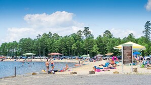 A beach with people swimming and sunbathing, umbrellas, and a signboard. - Pool Table-Hot springs Village Cozy Twnhse+Walk 2 lake (Hot Springs village)