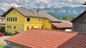 A yellow building with a red-tiled roof, surrounded by mountains. - Cozy vacation apartment (Ofterschwang)