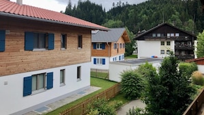 A residential area with wooden and white houses, a wooden fence, and a forested hill in the background. - Cozy vacation apartment (Ofterschwang)