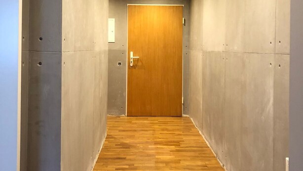 A hallway with a wooden door at the end, concrete walls, and a wooden floor. - Cozy vacation apartment (Ofterschwang)