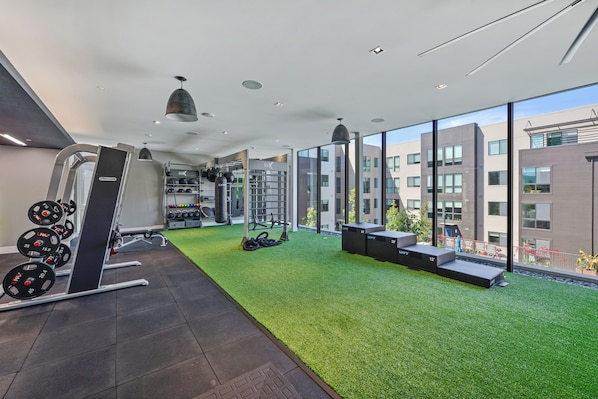 A gym with weightlifting equipment, a pull-up bar, and a green artificial turf area.