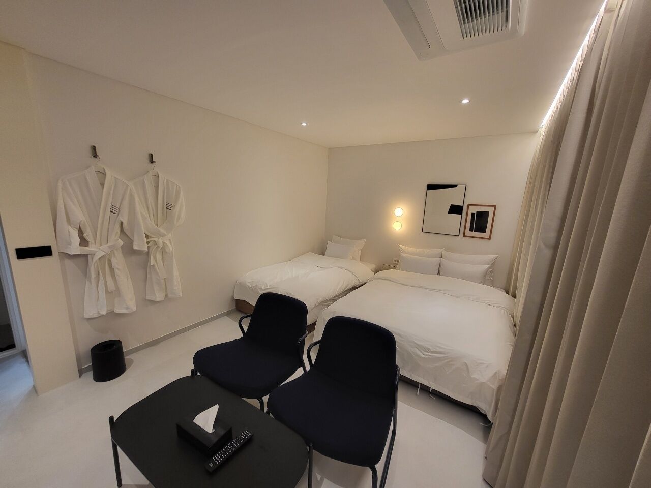 Habitación de hotel con dos camas, un escritorio con silla y un perchero en la pared.