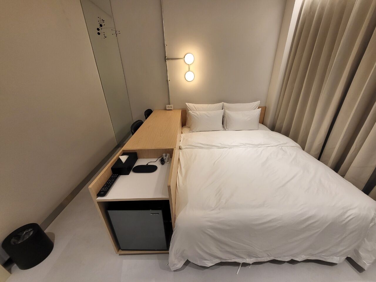 Une chambre d’hôtel équipée d’un lit, d’un bureau, d’une chaise, d’une petite armoire et d’une lampe fixée au mur.