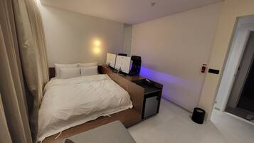 Una habitación de hotel moderna con una cama grande, mesitas de noche, un escritorio con una computadora y un pequeño cubo de basura.