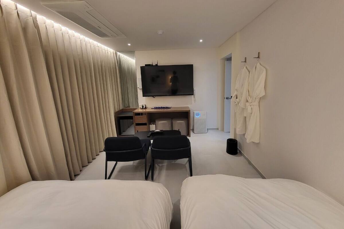 A hotel room with two beds, a desk with a chair, a TV, and a wardrobe with robes.
