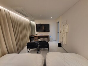 A hotel room with two beds, a desk with a chair, a TV, and a wardrobe with robes. - Anook hotel Osan Branch (Osan)