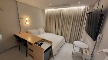 Habitación de hotel con cama, escritorio con silla, una mesita, televisor y teléfono.