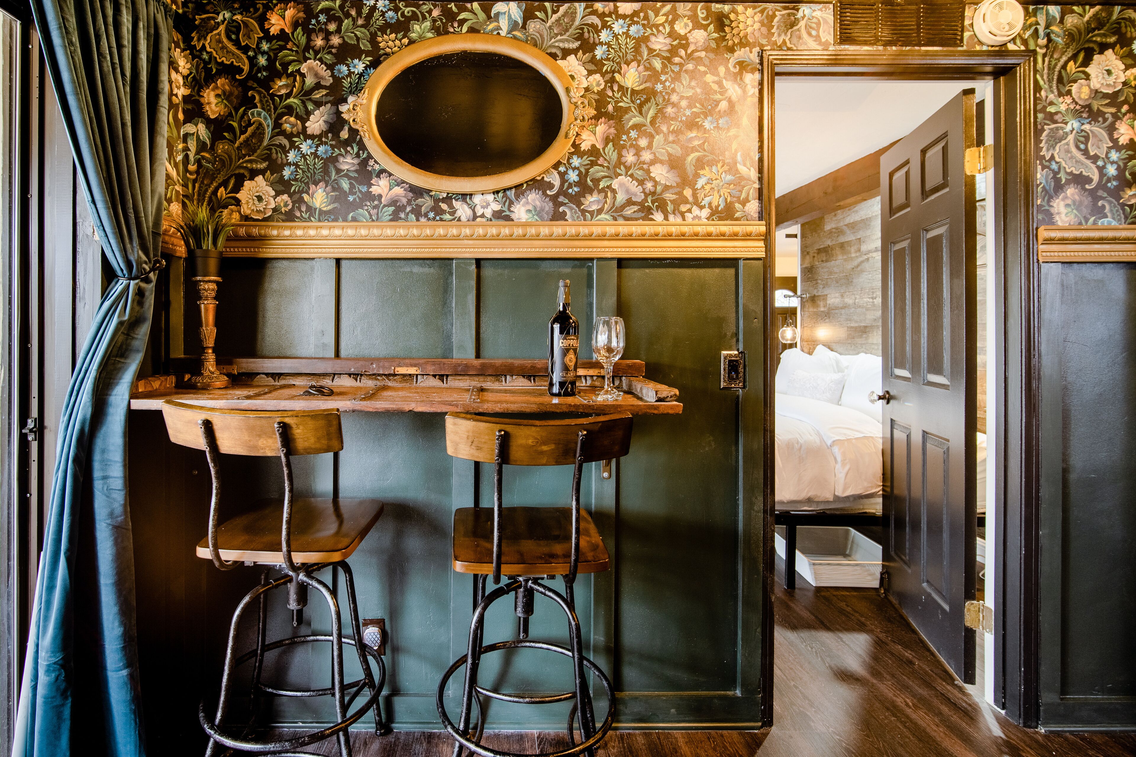 Un coin bar avec un comptoir en bois, deux tabourets et une bouteille de spiritueux.