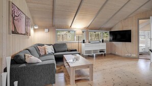 A modern living room with a grey sectional sofa, a wooden coffee table, a white desk, and a flat-screen TV mounted on the wall. - 3 bedroom cozy home in Højslev (Højslev)