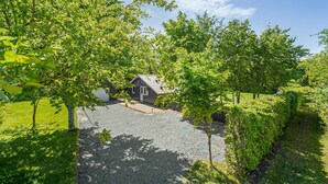 A small house with a gravel driveway, surrounded by lush greenery and trees. - 3 bedroom cozy home in Højslev (Højslev)