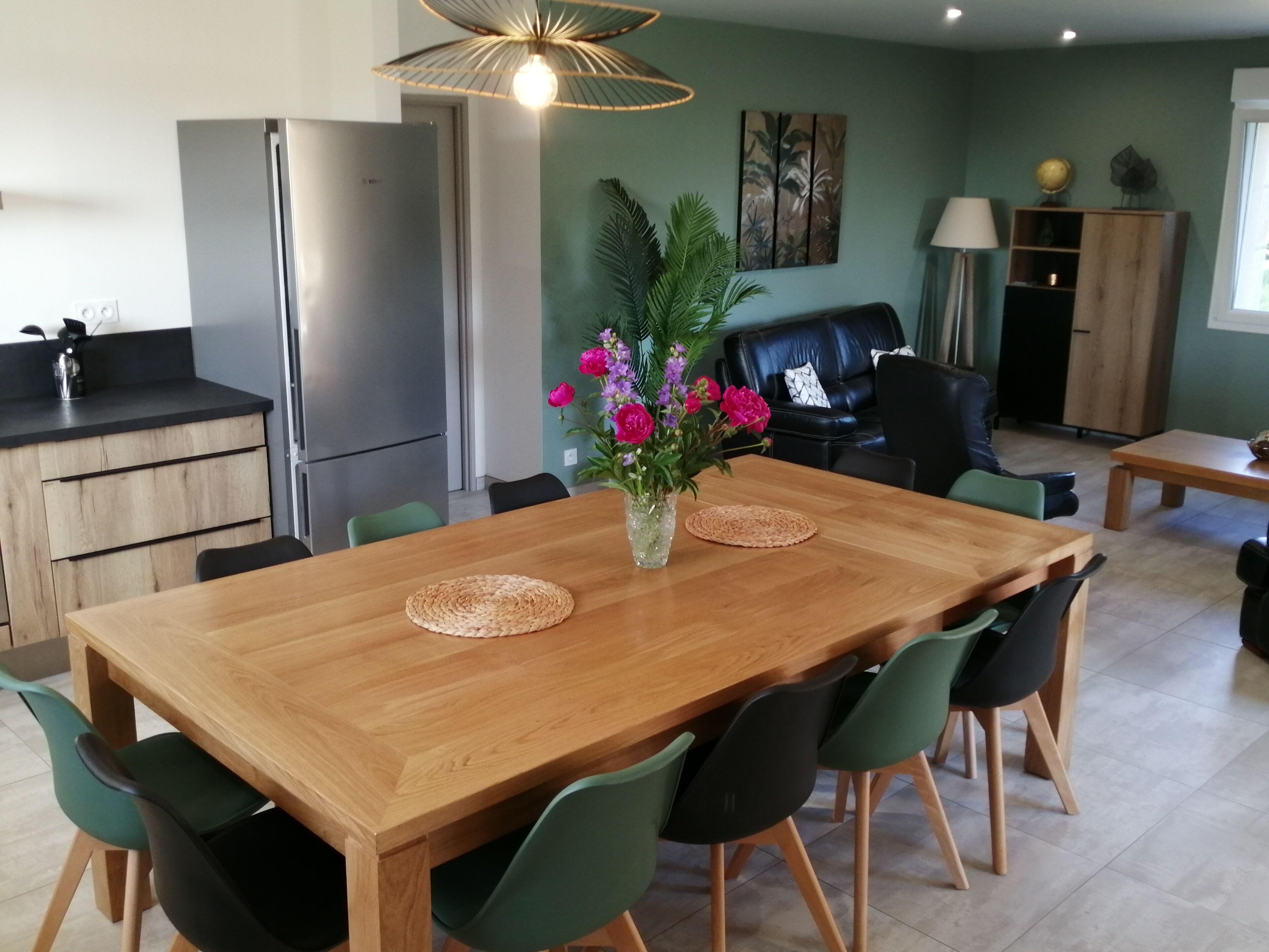 A modern kitchen with a stainless steel refrigerator, wooden cabinets, and a dining area with a wooden table and green chairs.