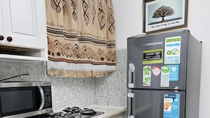 A compact kitchen with white cabinets, a microwave, a gas stove, a stainless steel refrigerator, and a tiled backsplash.