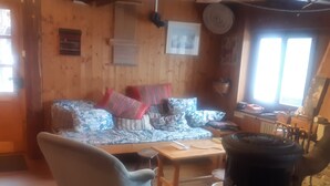 Ein gemütliches Zimmer mit Holzbalkendecke, einer Couch mit gemusterten Kissen, einem Sessel, einem Tisch und einem großen Heizkörper.