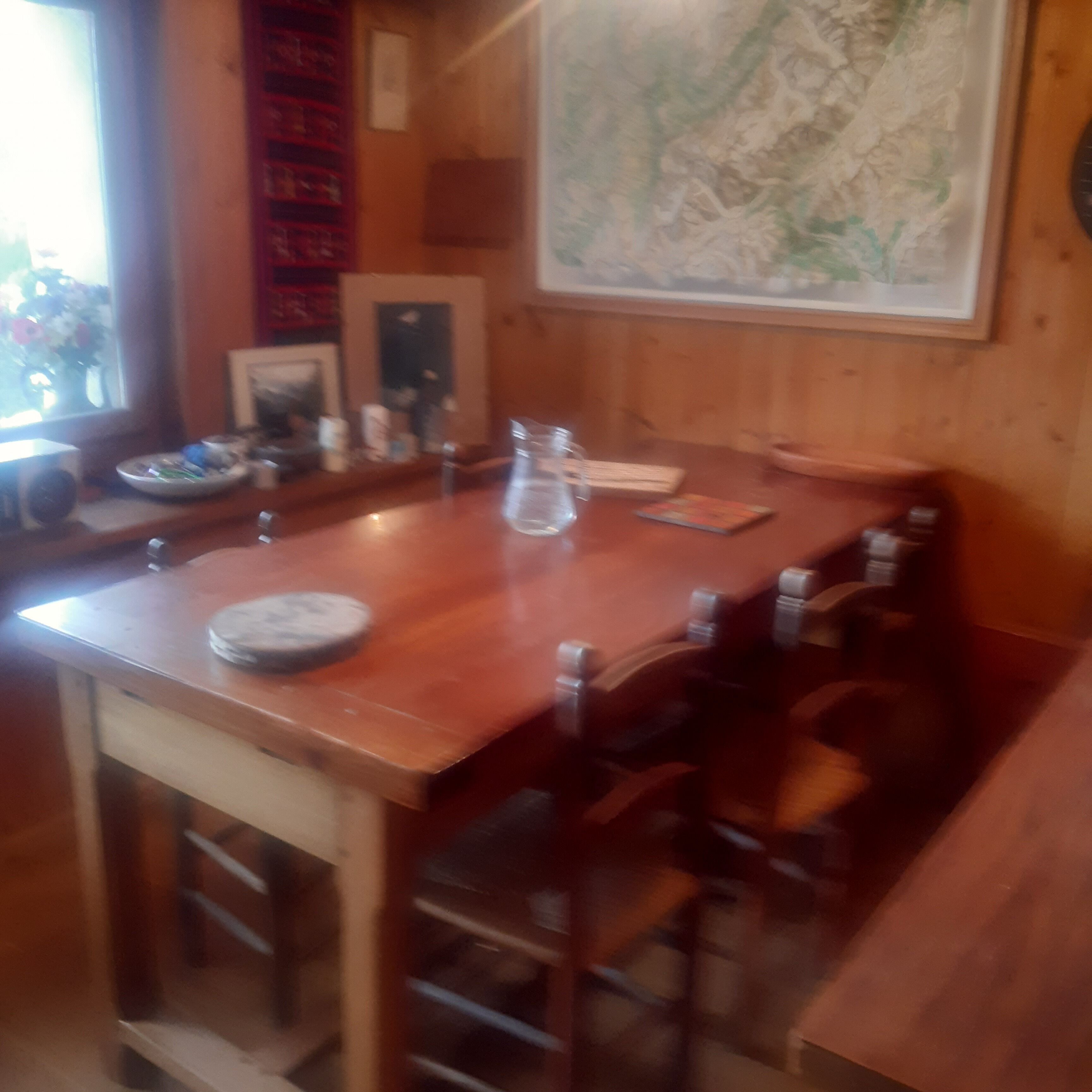 A wooden dining table with chairs, a small plate, a glass, and a framed picture on the wall.