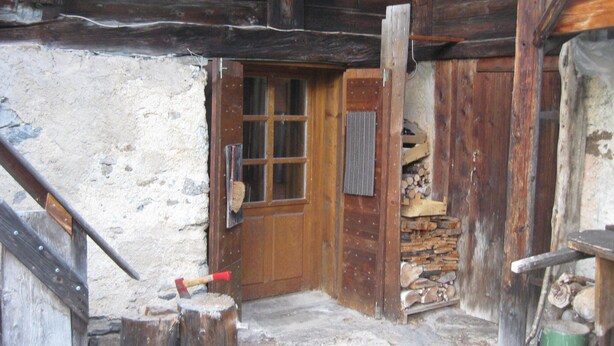 Eine rustikale Holztür mit Fenster, eine Holzbank und ein Holzstoß im Inneren eines Gebäudes.