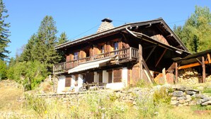 Ein rustikales Holzhaus mit einem Balkon, umgeben von einer Steinmauer und Wildblumen.