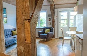 A room with a wooden ceiling, a blue sofa, a grey armchair, a white table, and a door with windows. - Awesome apartment in Gudhjem with WiFi (Gudhjem)
