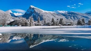 Lumipeitteinen vuoristomaisema, joka heijastuu kirkkaasti jäätyneen järven pinnasta.