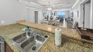 A spacious kitchen with granite countertops, stainless steel sinks, and a dining area with a view of the ocean. - Ocean Ritz 1503 • Luxury Beachfront Retreat (Panama City Beach)