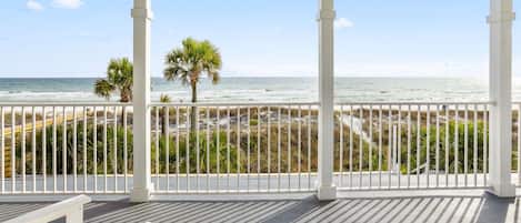 A covered balcony with a view of the beach and ocean.