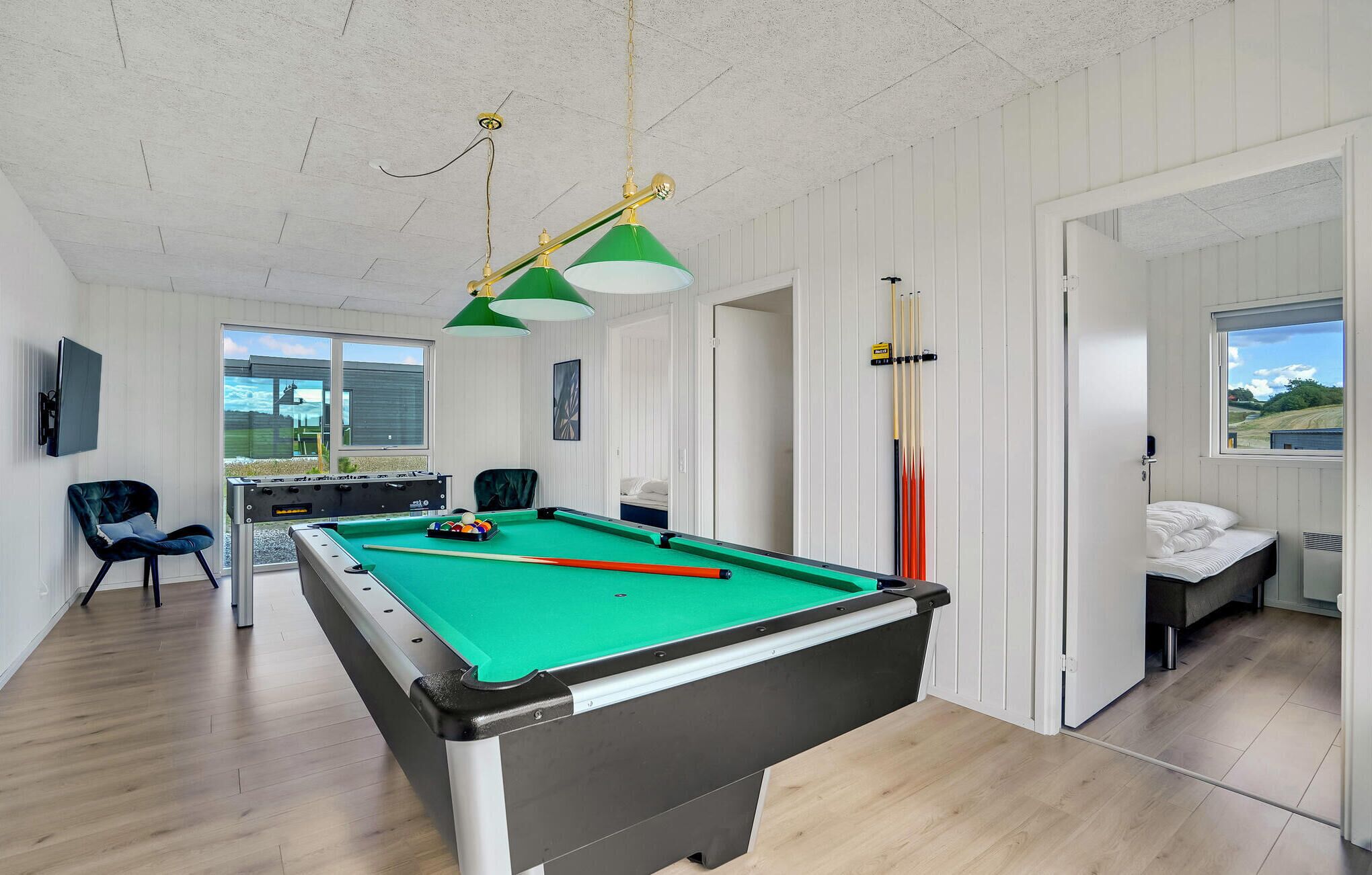 A pool table with a green felt surface, two chairs, a bed, and a window with a view of a landscape.