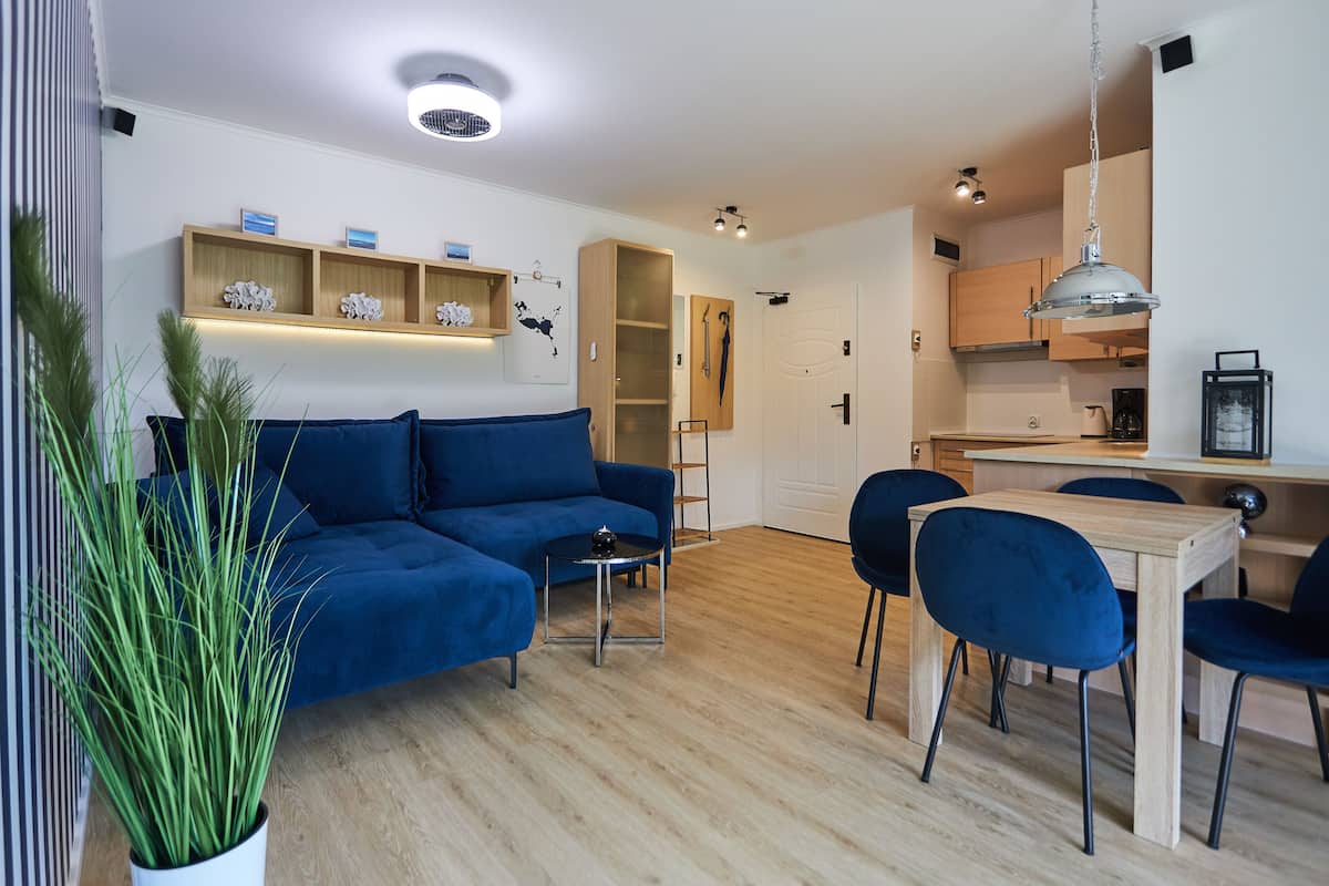 Ein modernes Wohnzimmer mit einem blauen Sofa, einem Esstisch mit Stühlen und einer Küchenzeile mit Holzschränken.
