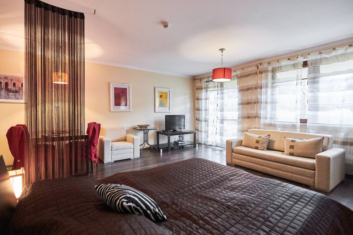 Ein modernes Hotelzimmer mit einem großen Bett, einer Couch, einem Fernseher und einem Vorhang mit Streifenmuster.