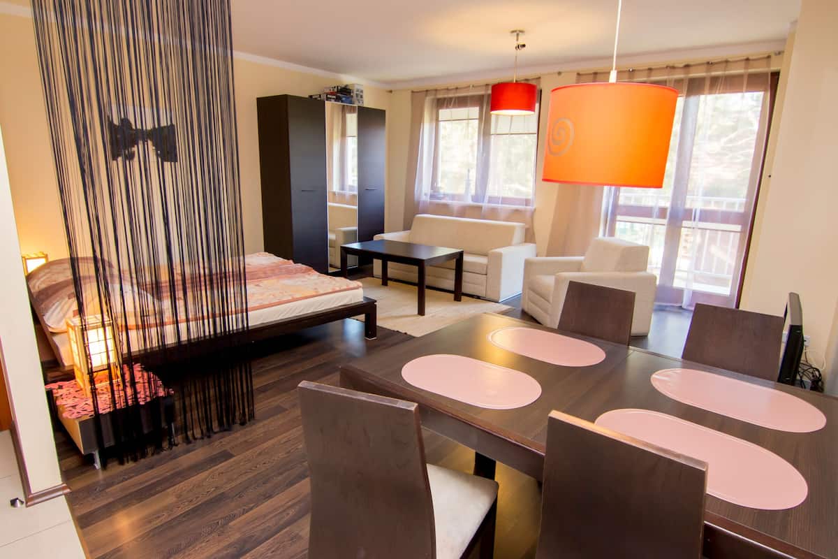 Ein modernes Hotelzimmer mit Bett, Esstisch mit Stühlen, einer Couch und einem großen Fenster mit Vorhängen.