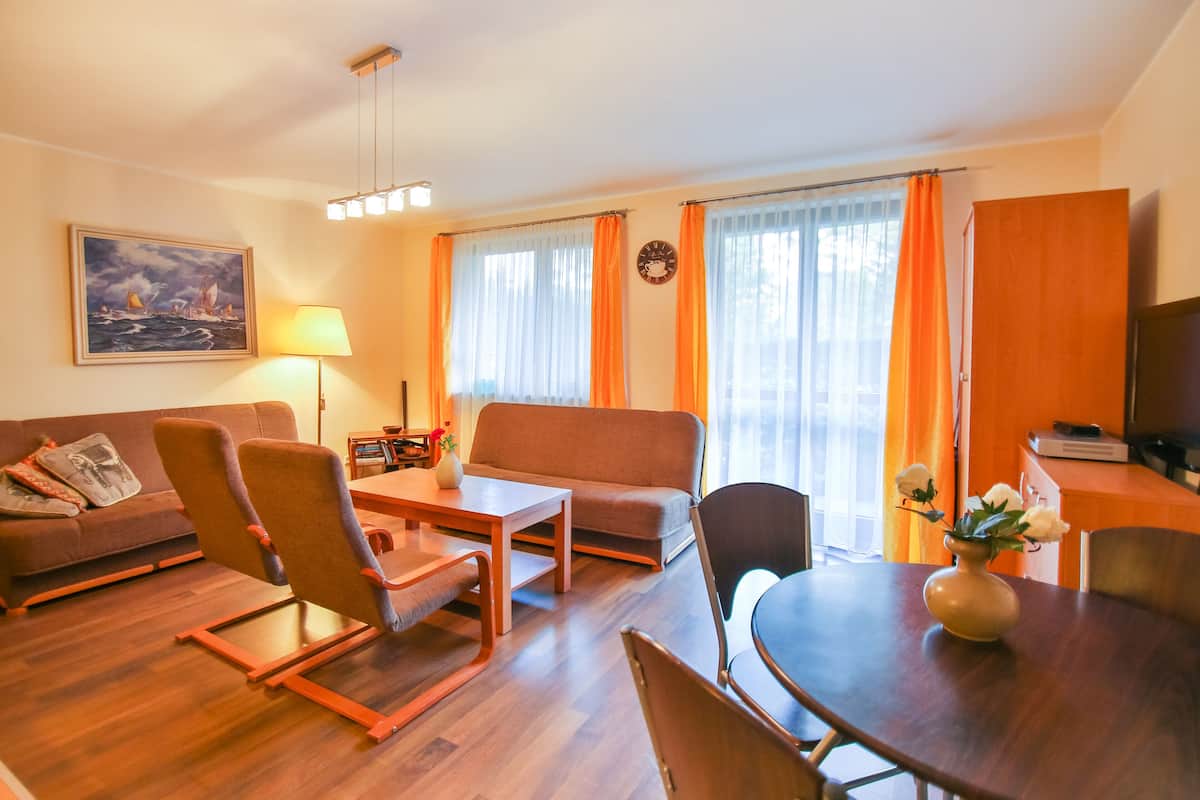 Ein Wohnzimmer mit Sofa, Sesseln, Esstisch und Fernseher.