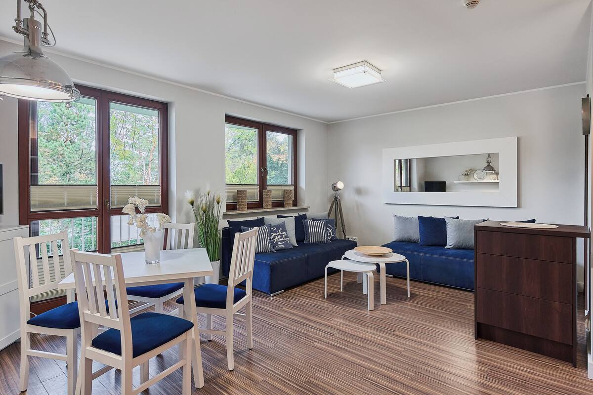 Ein modernes Wohnzimmer mit Essbereich, einem blauen Sofa, Holzstühlen und einer Kücheninsel.