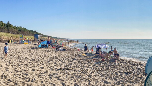 A beach with people sunbathing, swimming, and playing. There are umbrellas, beach chairs, and a lifeguard tower. - 2 bedroom amazing apartment in Bobolin (Bobolin)