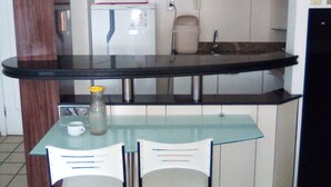 A compact kitchen with a glass table and two chairs, a microwave, a refrigerator, and a sink. - Silva Hospedagem - Flat Number One (São Luís)