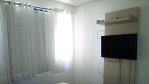 A bedroom with a bed, a TV mounted on the wall, and a window with curtains. - Silva Hospedagem - Flat Number One (São Luís)