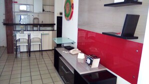 A compact kitchen with a microwave, a refrigerator, a dining table with chairs, and a red accent wall. - Silva Hospedagem - Flat Number One (São Luís)