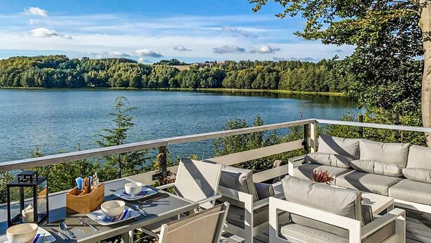 Un balcón con vistas a un lago, mobiliario exterior y zona de comedor.