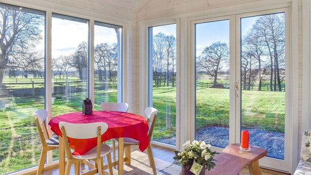 A dining area with a table set for four, large windows, and a view of a grassy landscape. - Lovely home in Skivarp with WiFi (Skivarp)
