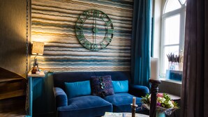 A cozy living room with a blue sofa, a round coffee table, and a wall clock. - Unique cosy Petite Maison with luxury jacuzzi (Hesdin)