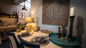 A dining area with a wooden table, chairs, a decorative wall piece, and a teal tray with a candle. - Unique cosy Petite Maison with luxury jacuzzi (Hesdin)