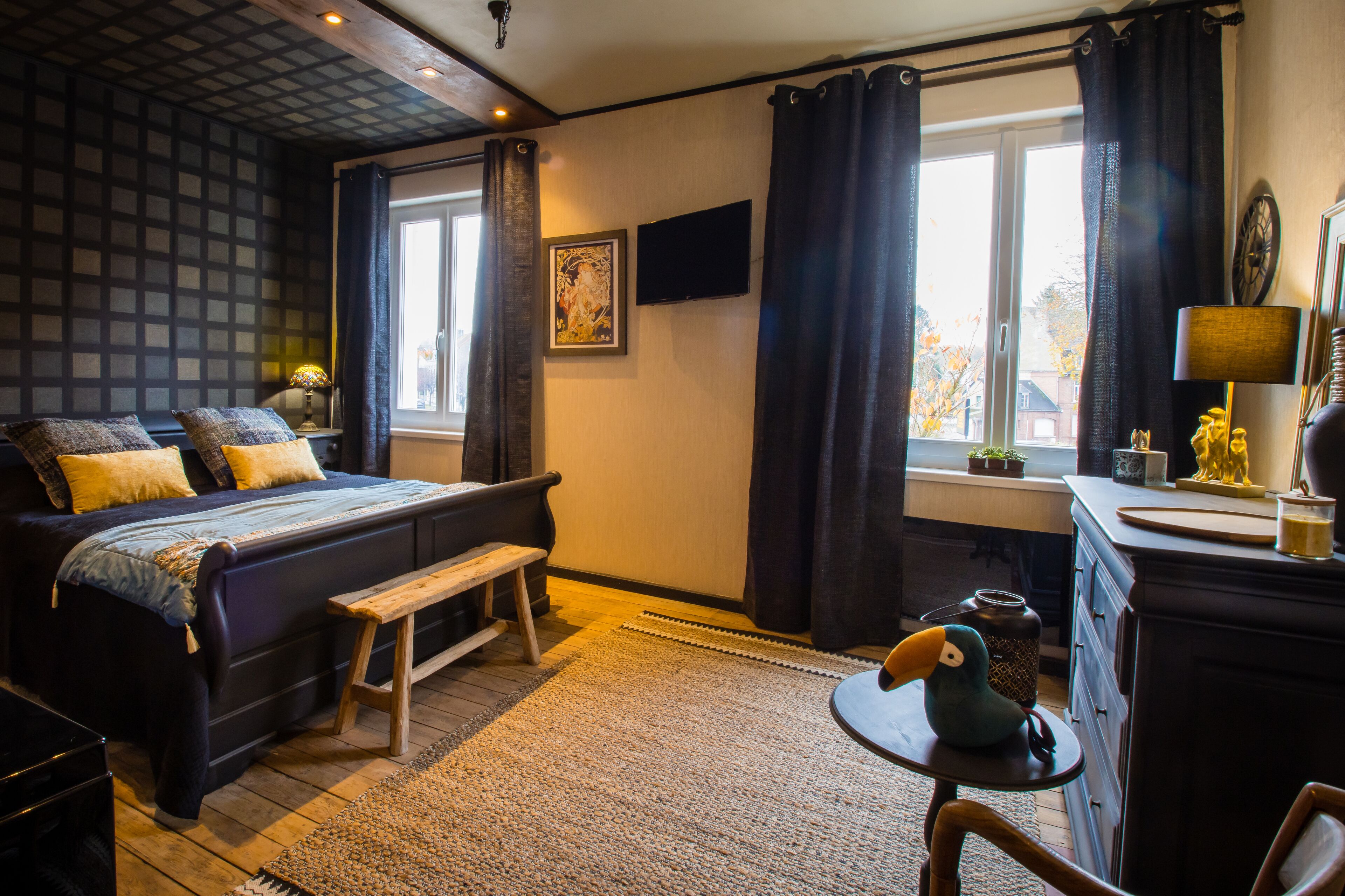 A bedroom with a bed, a bench, a desk, a lamp, and a window with curtains.