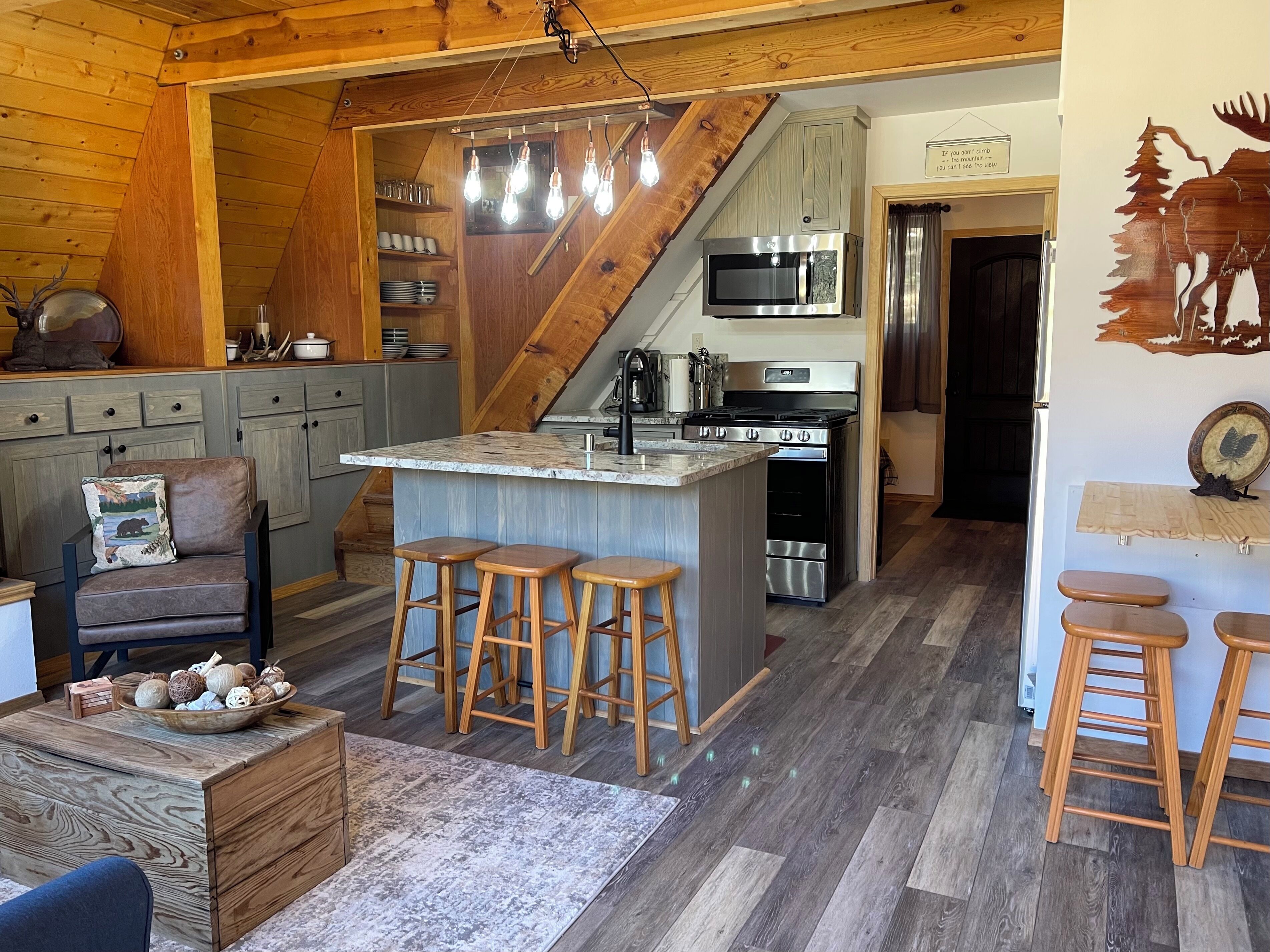 Una cocina acogedora con techo de madera, una isla central con taburetes y una escalera que lleva a otro nivel.