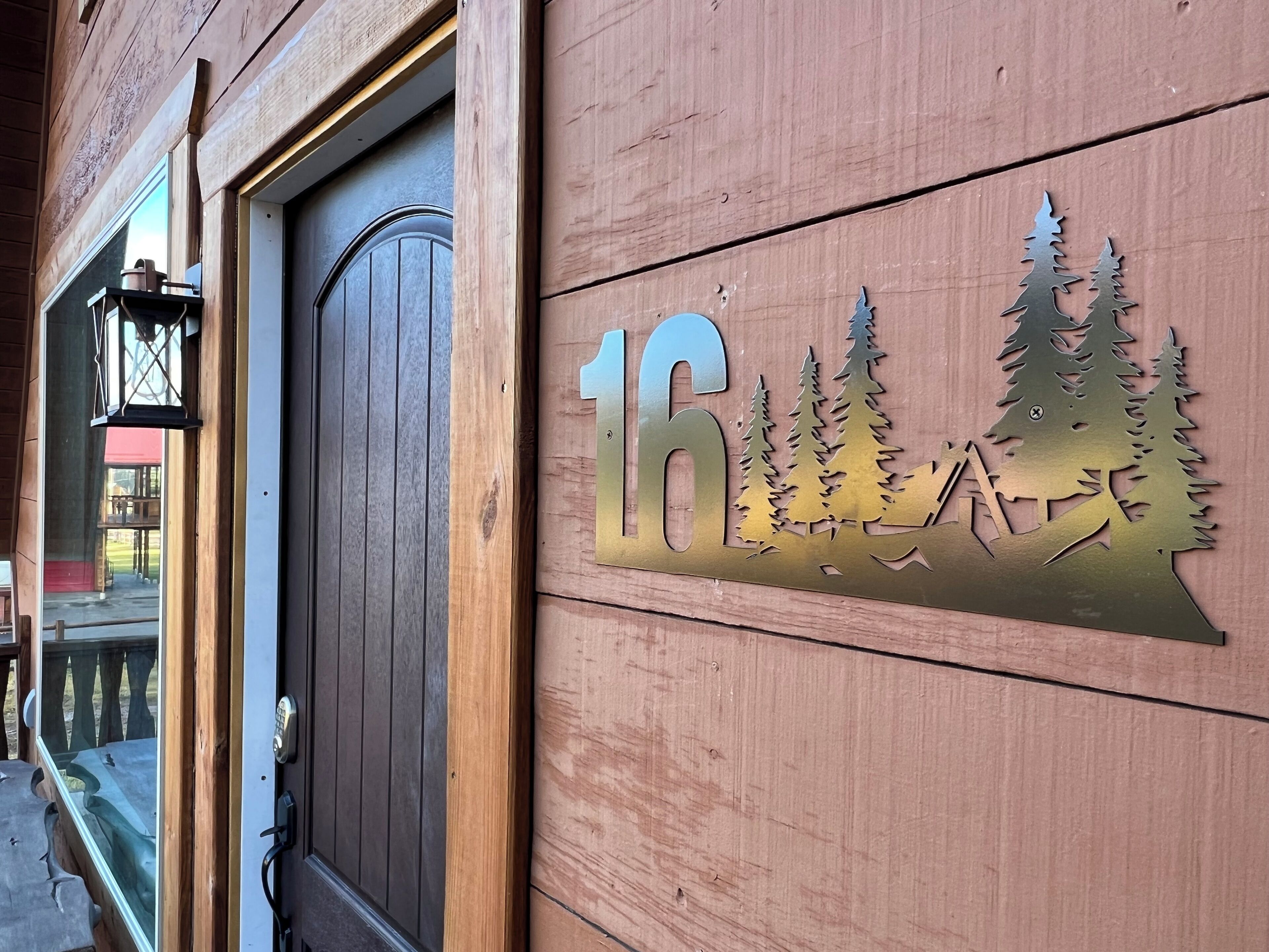 Puerta de madera con el número 16 y un corte decorativo con paisaje de montaña.