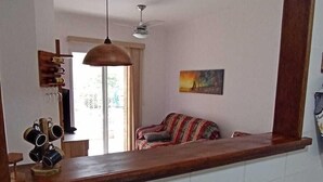 Ett kök med en bänkskiva i trä, en hängande taklampa, en takfläkt och ett fönster med utsikt över ett rum med en soffa.